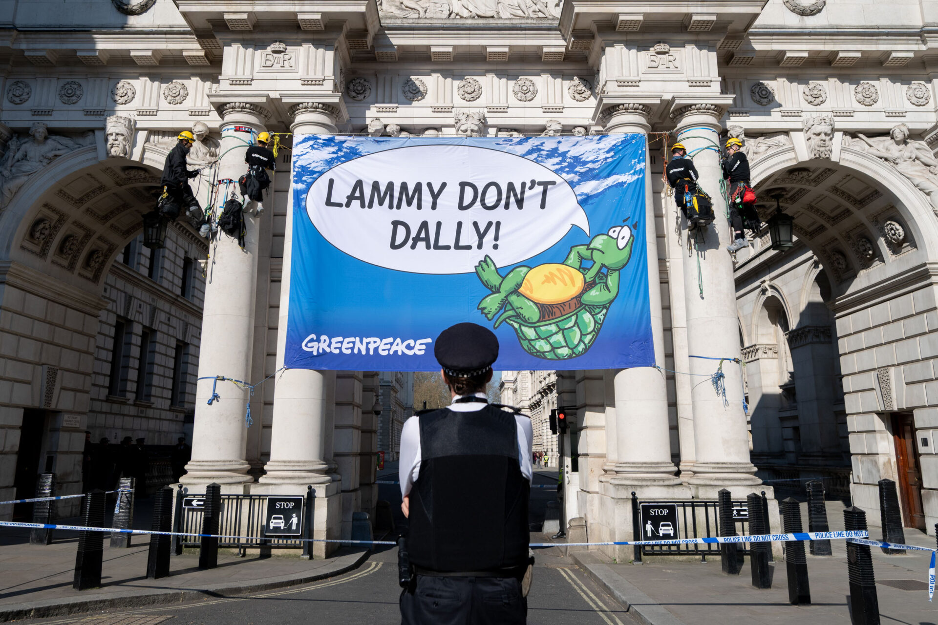 Un policier regarde une bannière avec une tortue et une bulle de discours disant "Lammy ne Dally pas".