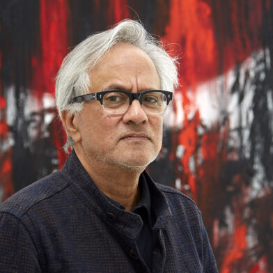 La tête d'Anish Kapoor devant une toile noire et rouge.